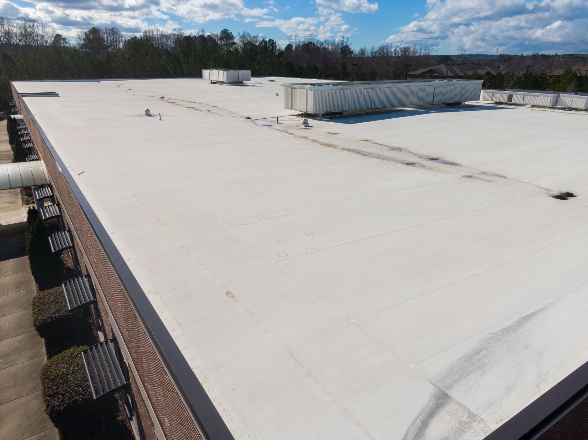 Flat commercial roof with white membrane, vents, and a blue sky.