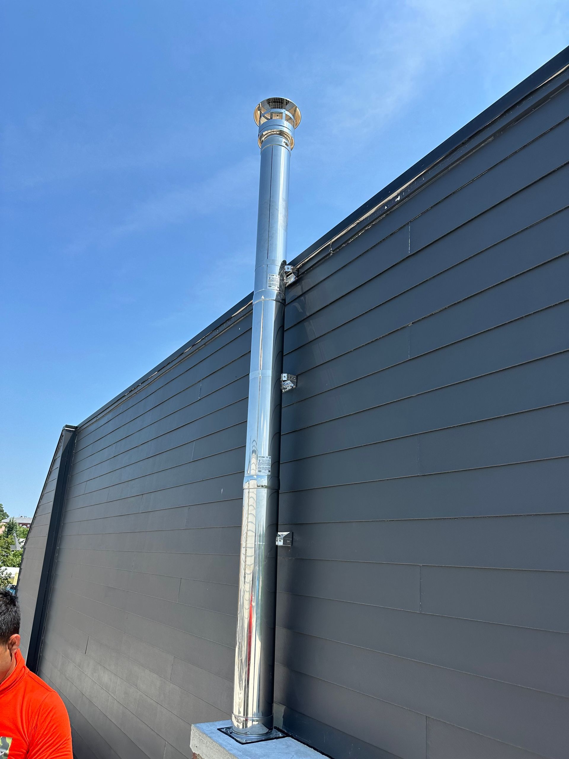 A man is standing next to a stainless steel chimney on the side of a building.