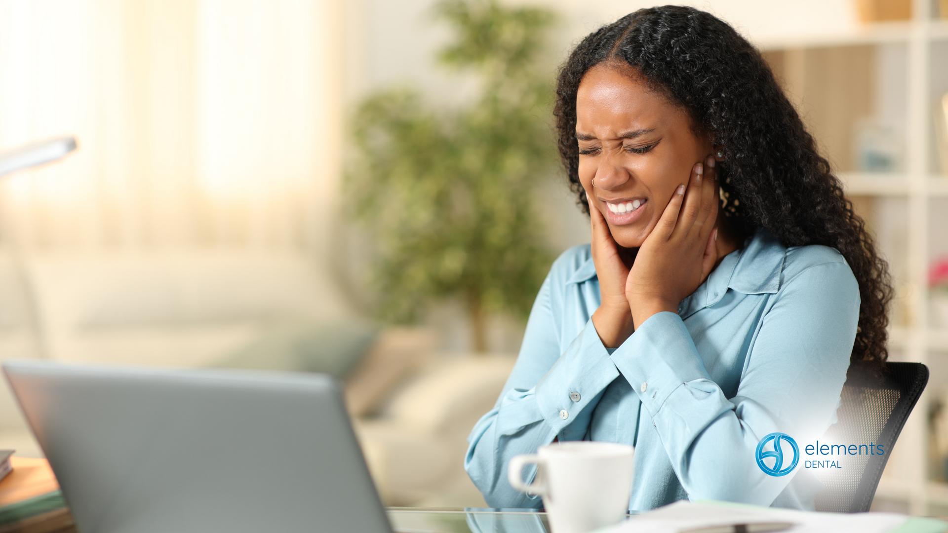 A woman is sitting at a desk with a laptop and a cup of coffee.