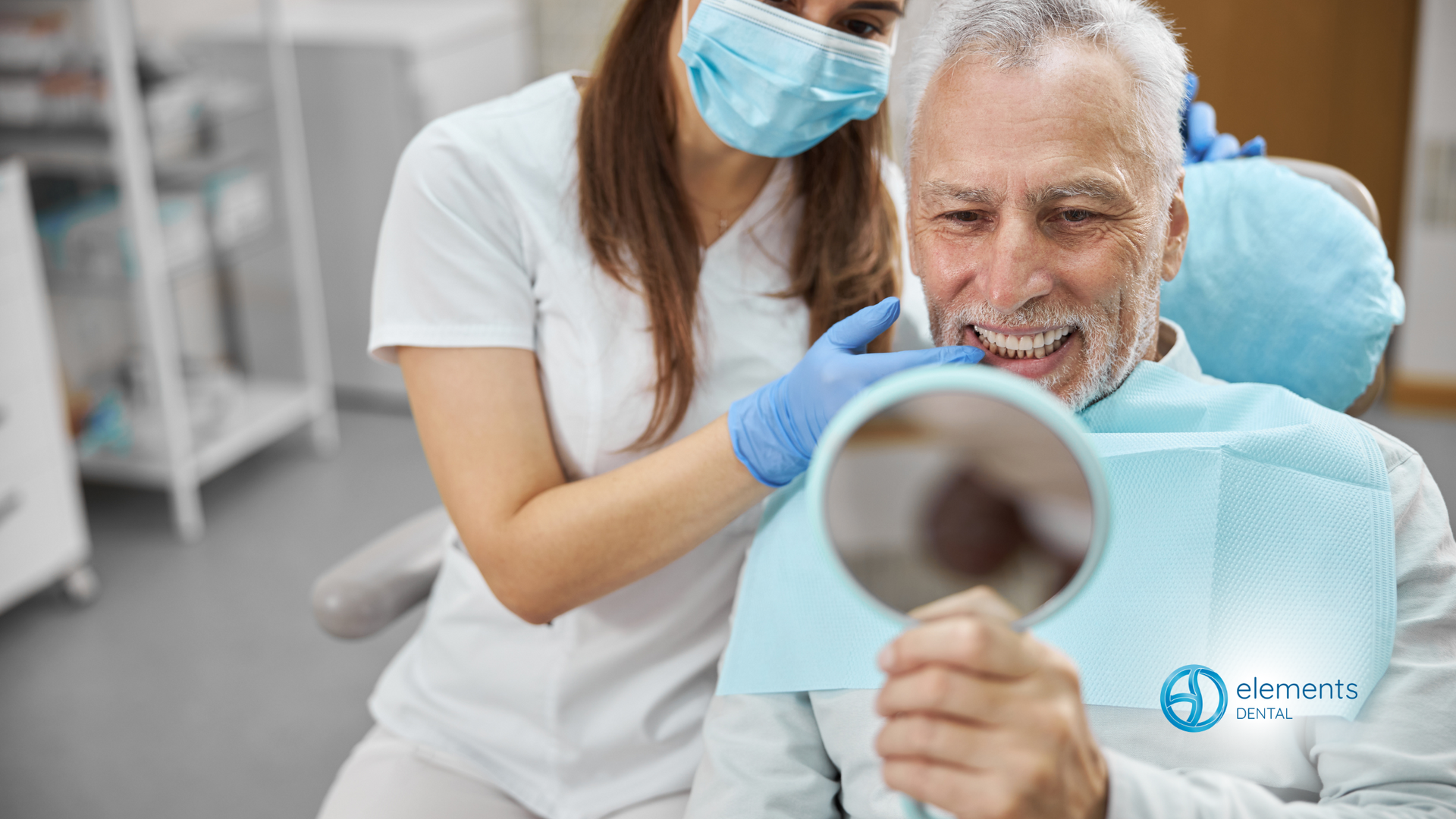 A man is sitting in a dental chair looking at his teeth in a mirror.