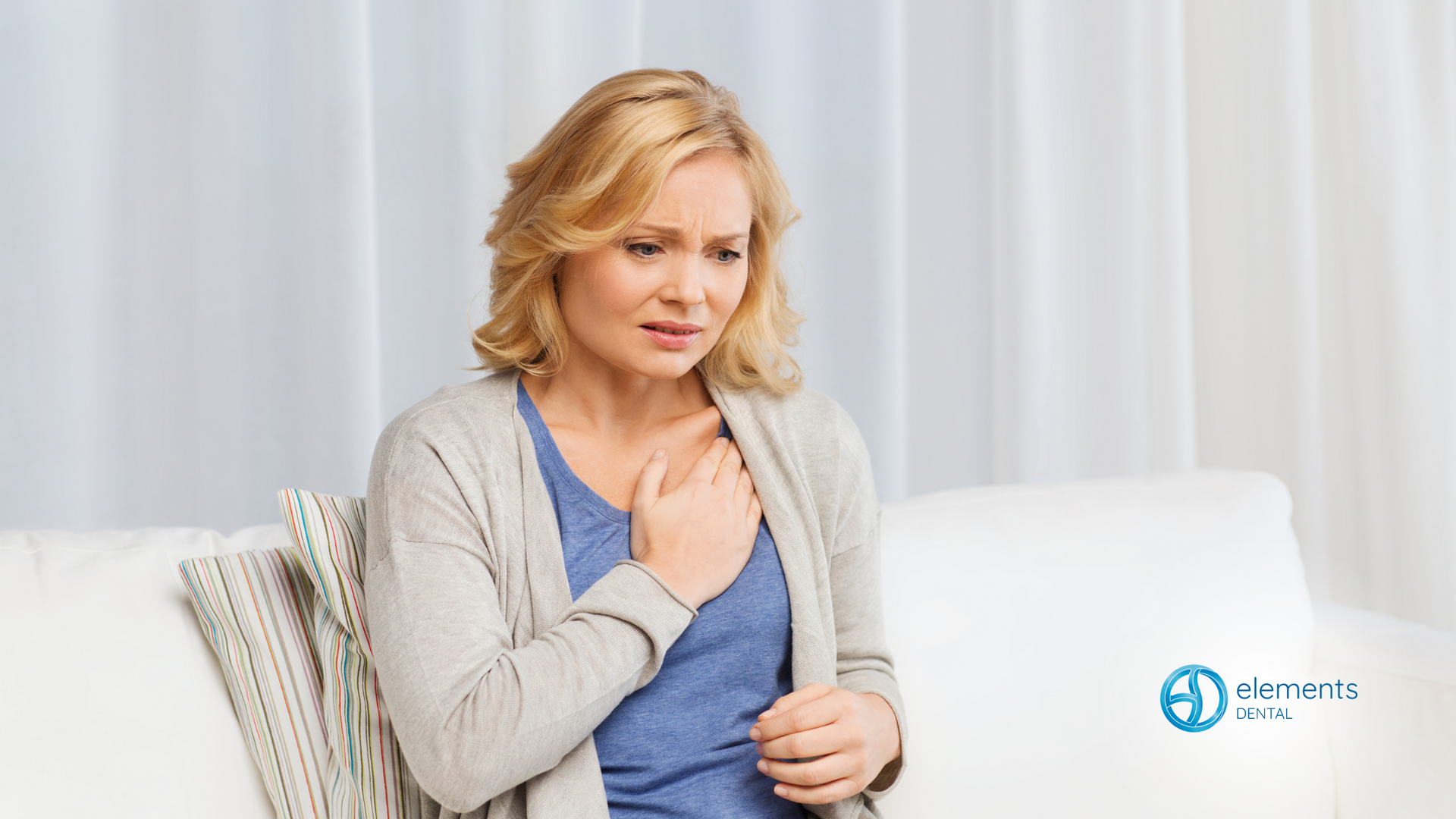 A woman is sitting on a couch with her hand on her chest.