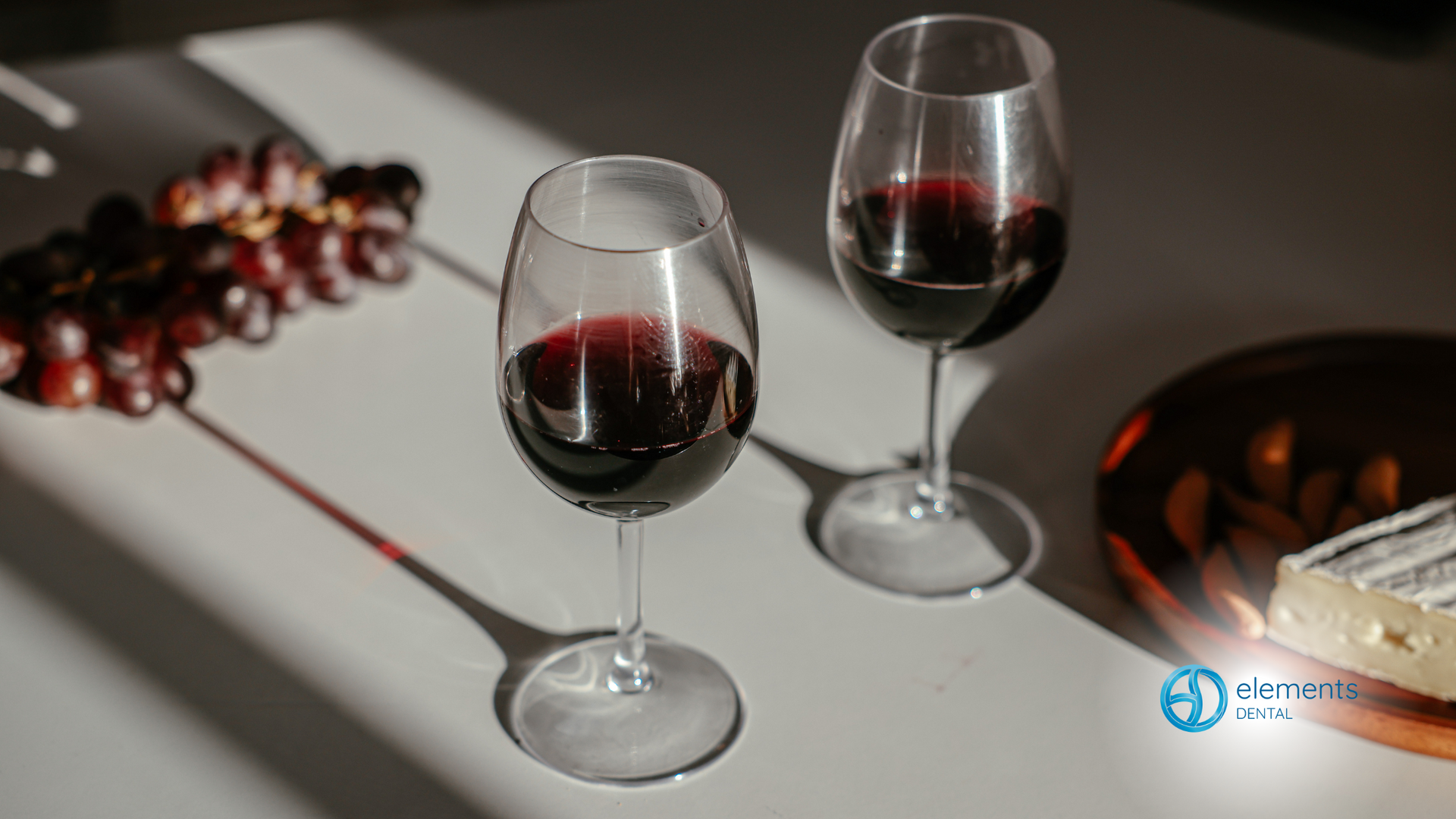 Two glasses of red wine are sitting on a table next to a bunch of grapes.