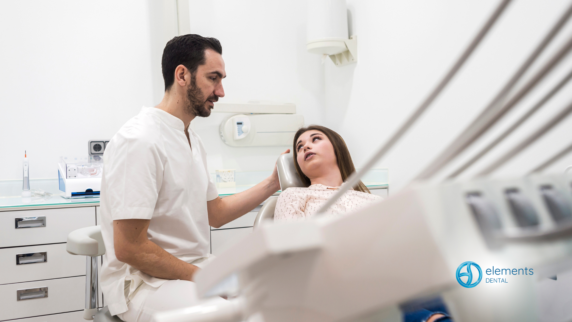 A dentist is talking to a patient in a dental chair.
