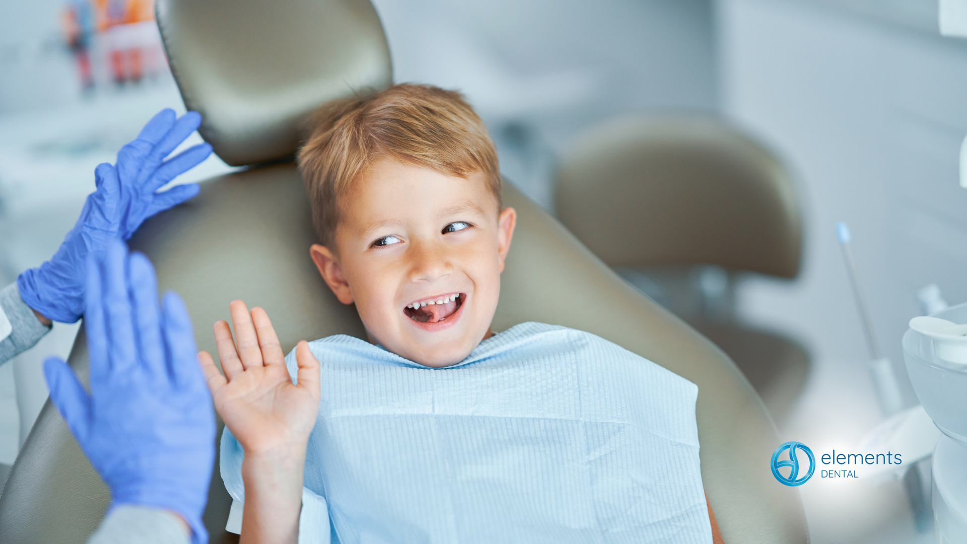 A young boy is sitting in a dental chair giving the dentist a high five.