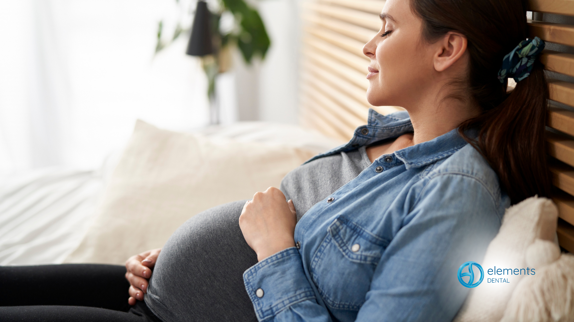 A pregnant woman is sitting on a bed holding her belly.