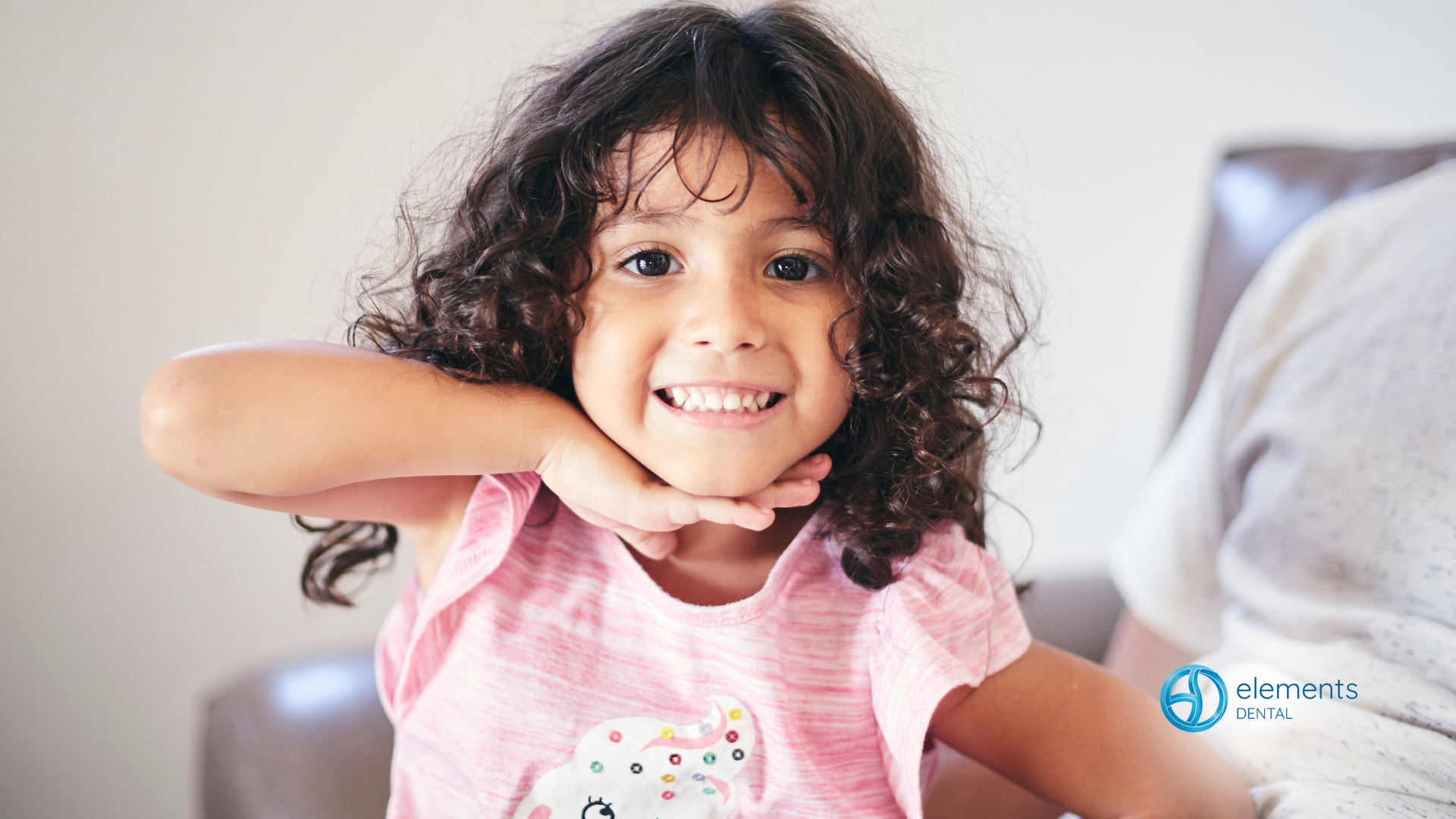 A little girl with curly hair is smiling for the camera.