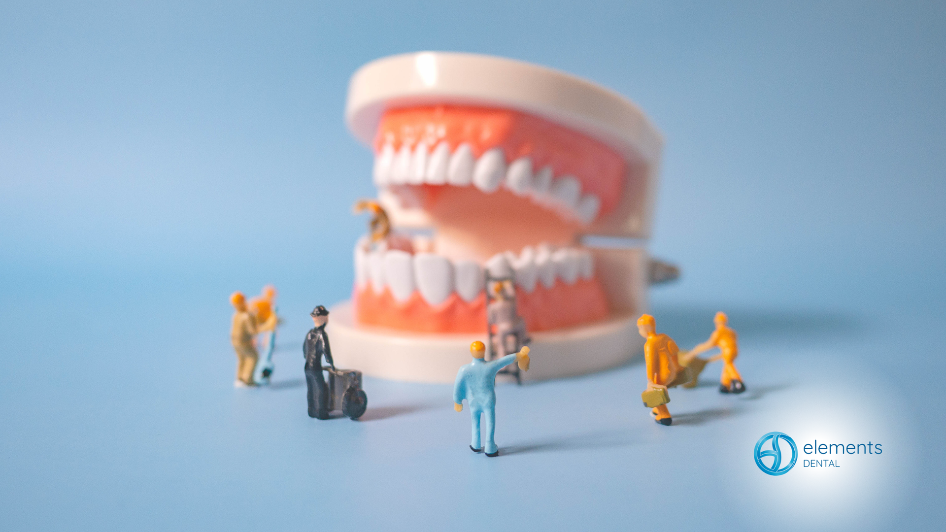 Miniature figures around a model of teeth, on a blue surface.