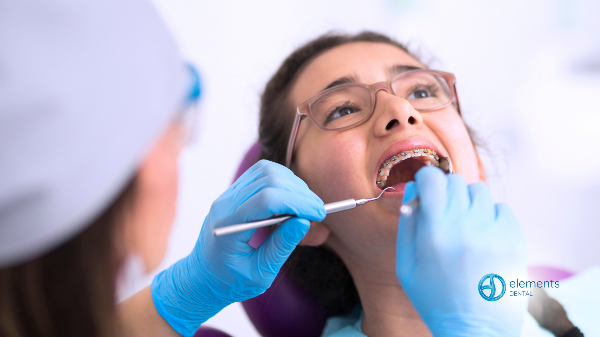 A woman with braces is getting her teeth examined by a dentist.