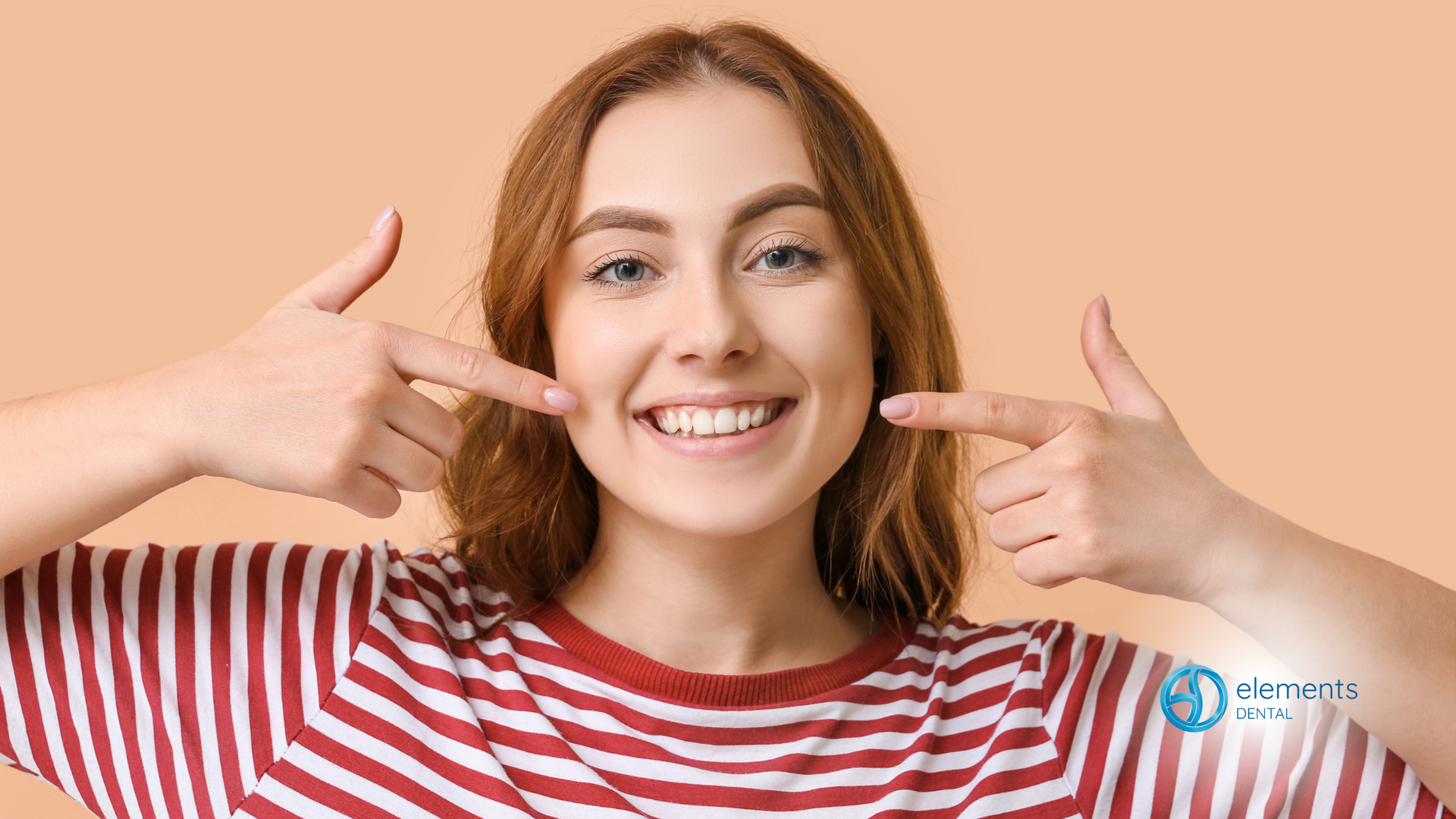 A woman in a striped shirt is smiling and pointing at her teeth.
