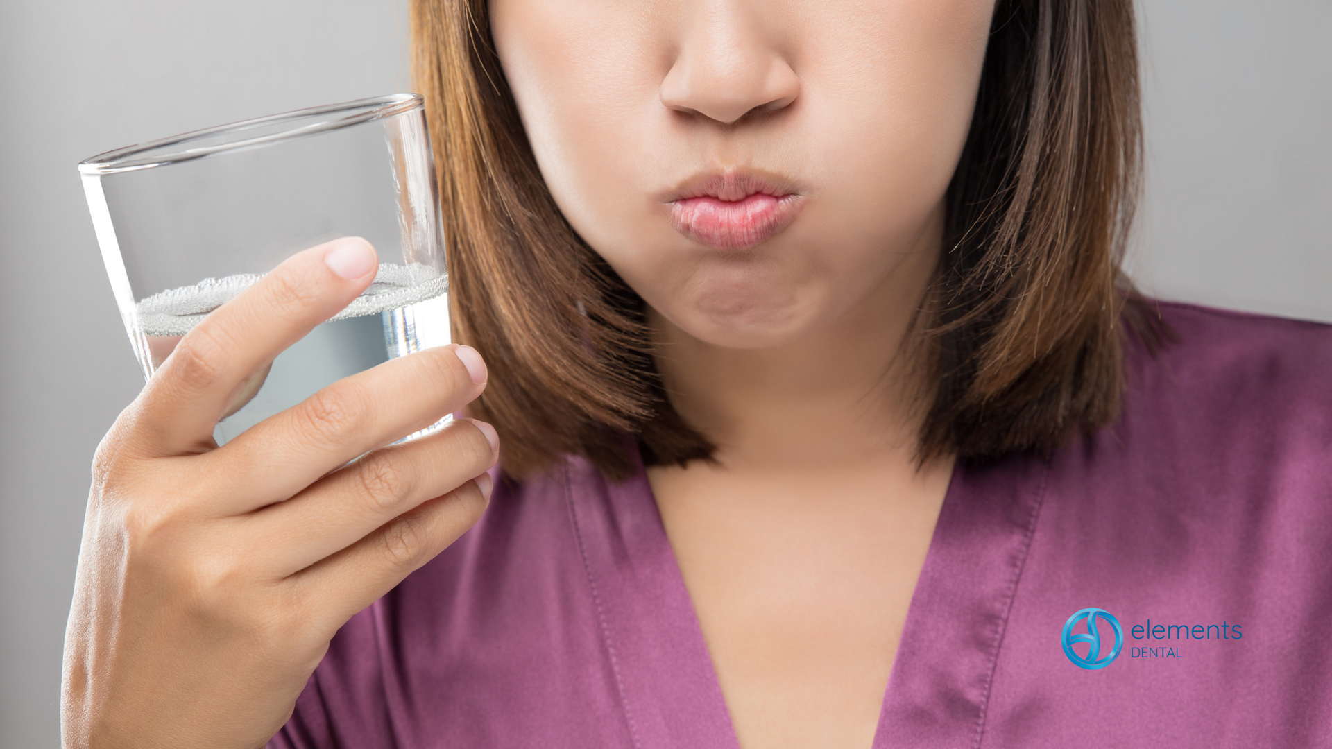 A woman is holding a glass of water in front of her mouth.