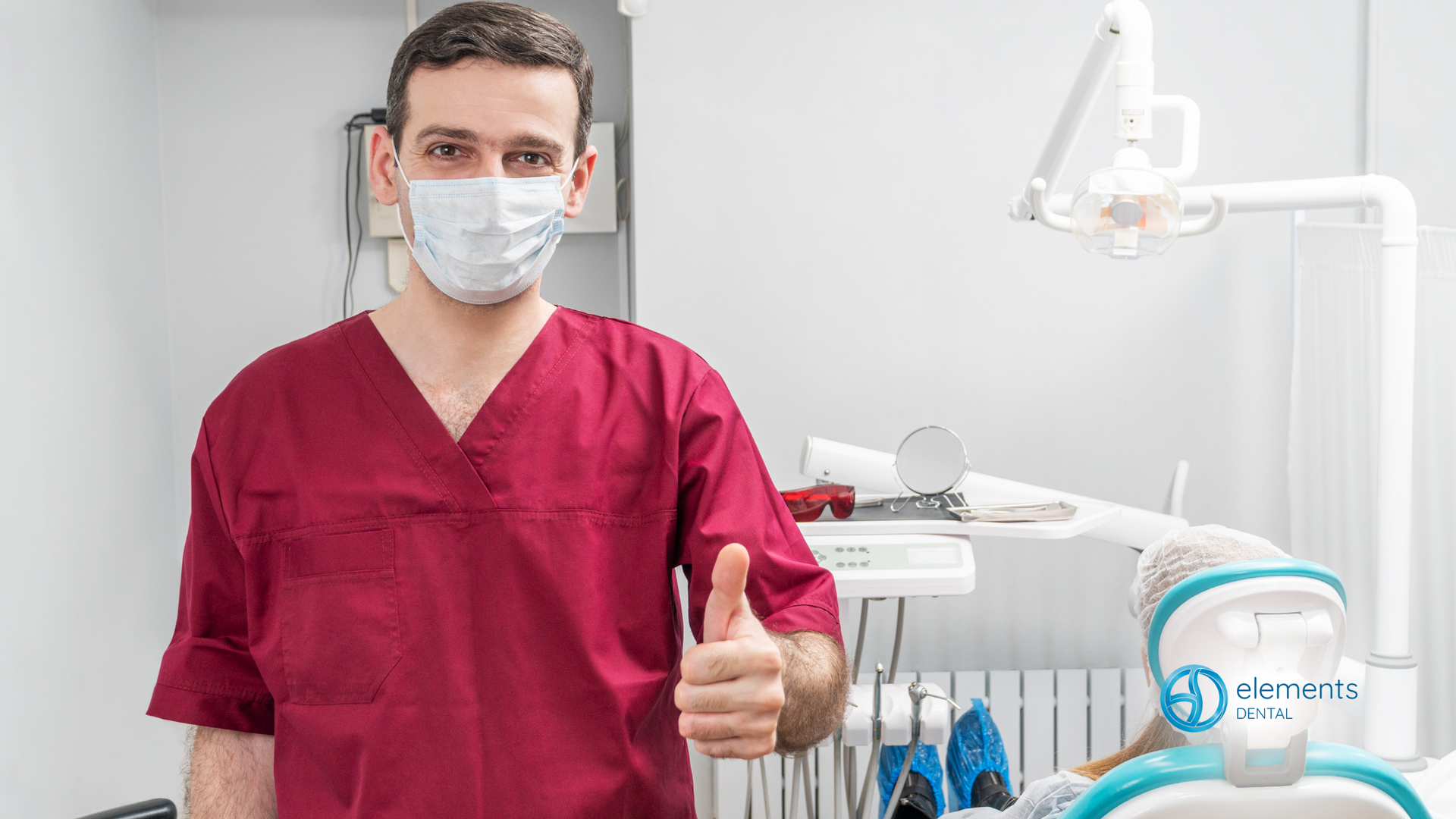 A dentist wearing a mask is giving a thumbs up in a dental office.