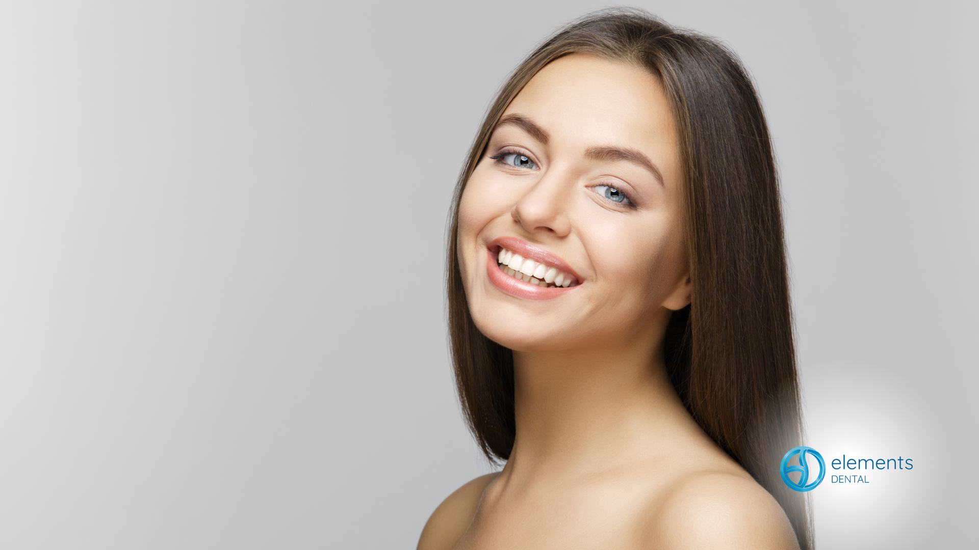 Woman with long brown hair smiling against a gray background.