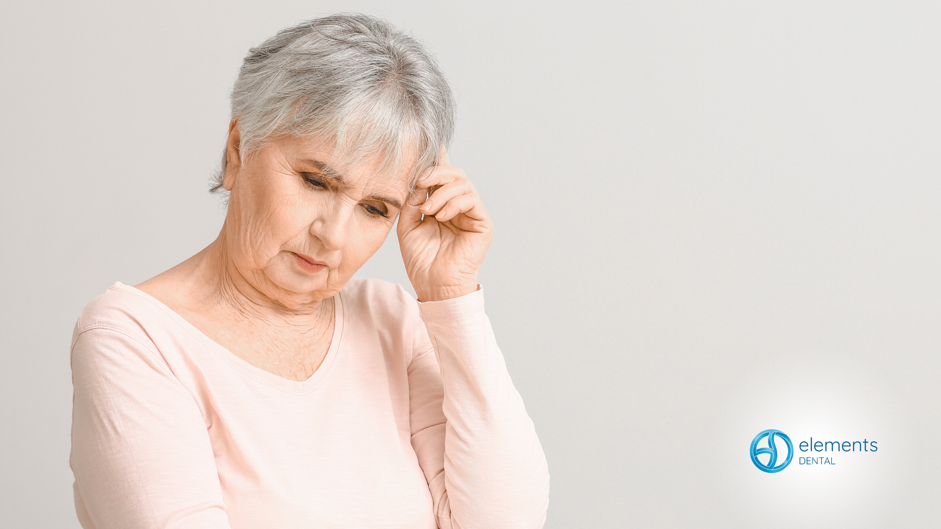 An elderly woman with gray hair is holding her head.