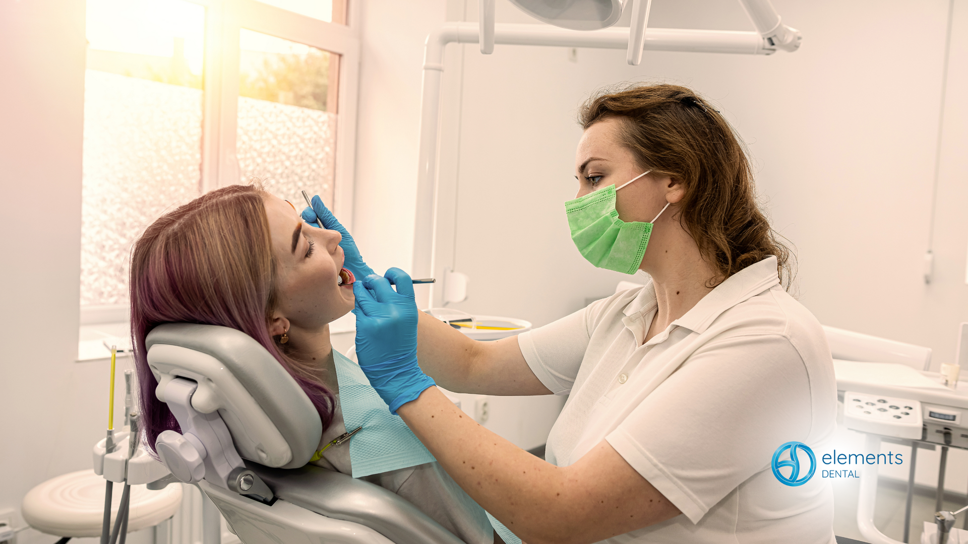 A woman is sitting in a dental chair while a dentist examines her teeth.