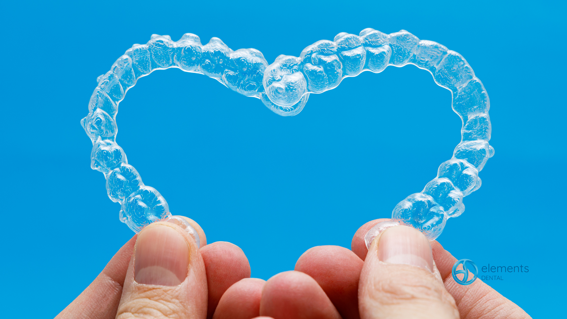 A person is holding a clear retainer in the shape of a heart.