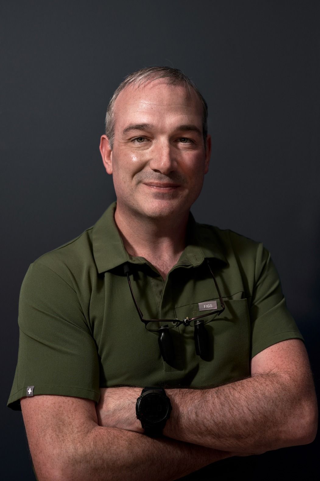 A man wearing a green shirt and glasses is standing with his arms crossed.