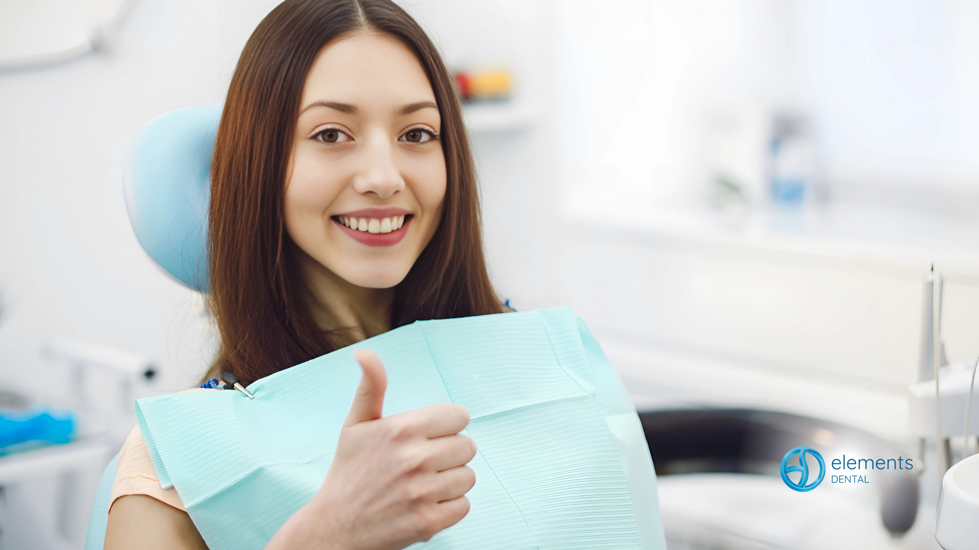 A woman is sitting in a dental chair giving a thumbs up.