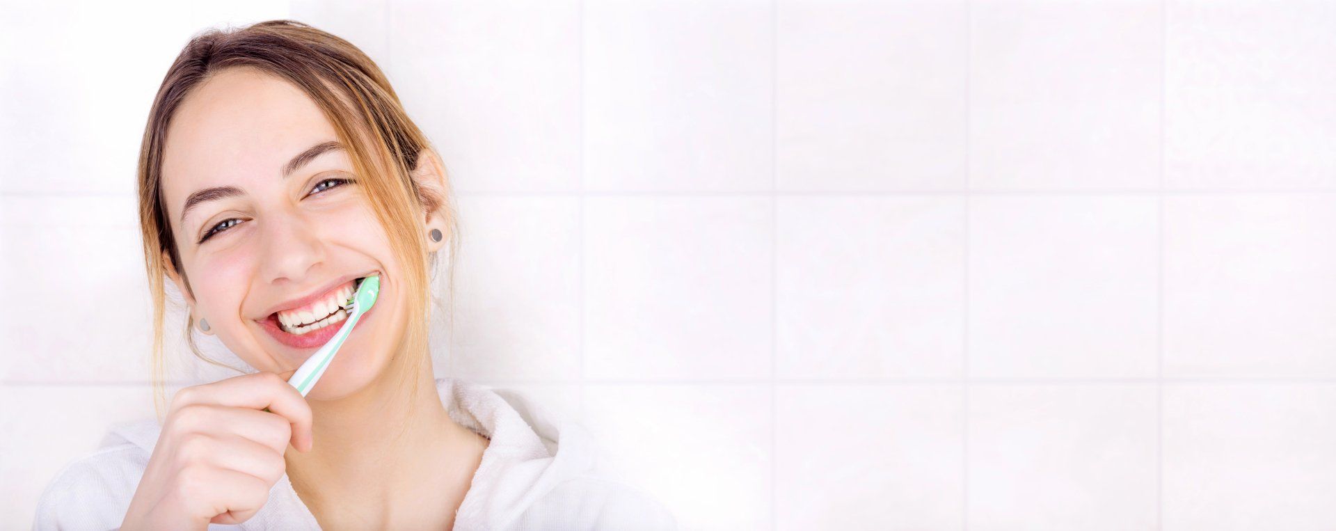 A woman is brushing her teeth in a bathroom and smiling.