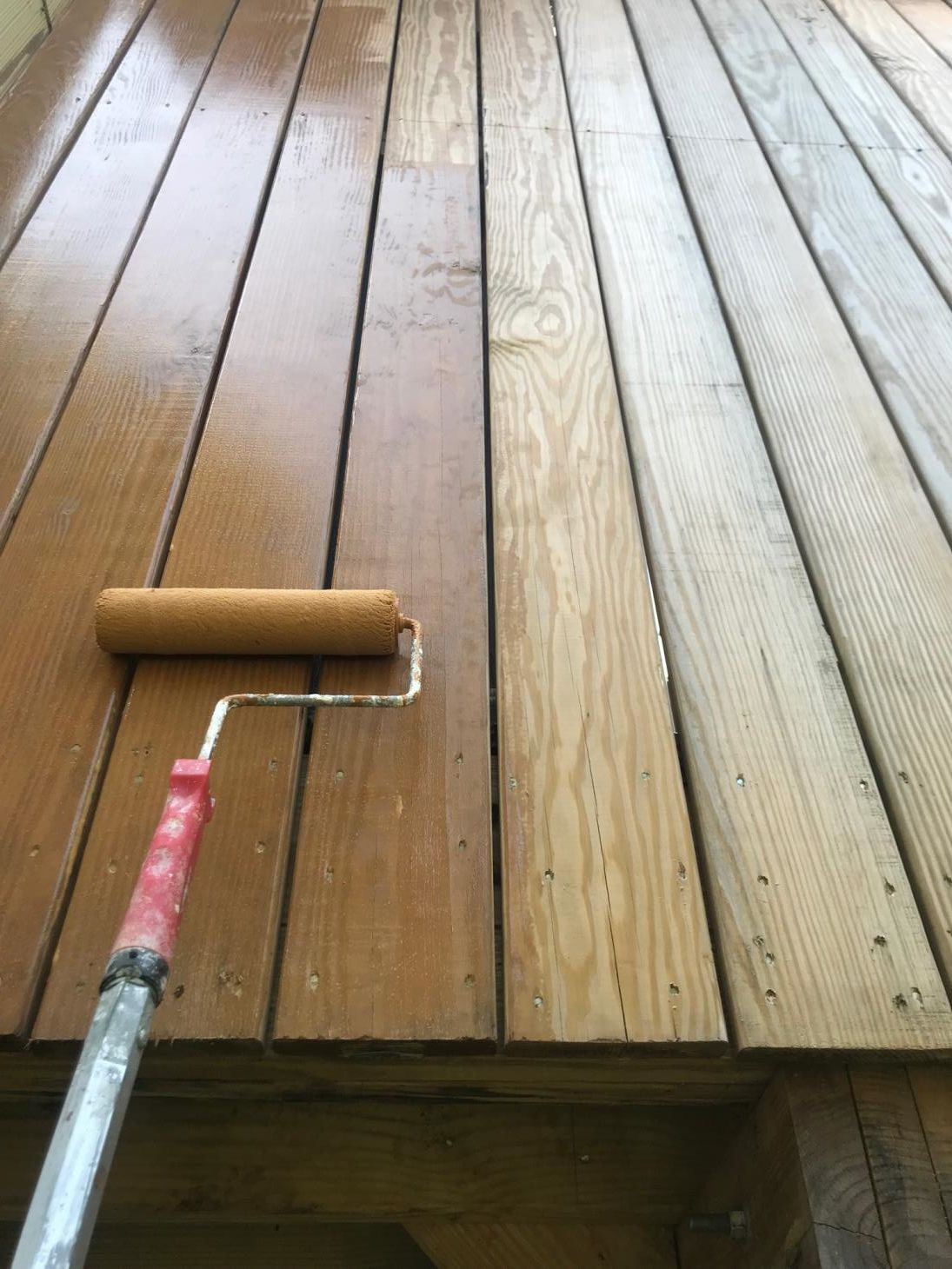 A person is sanding a wooden deck with a sander.