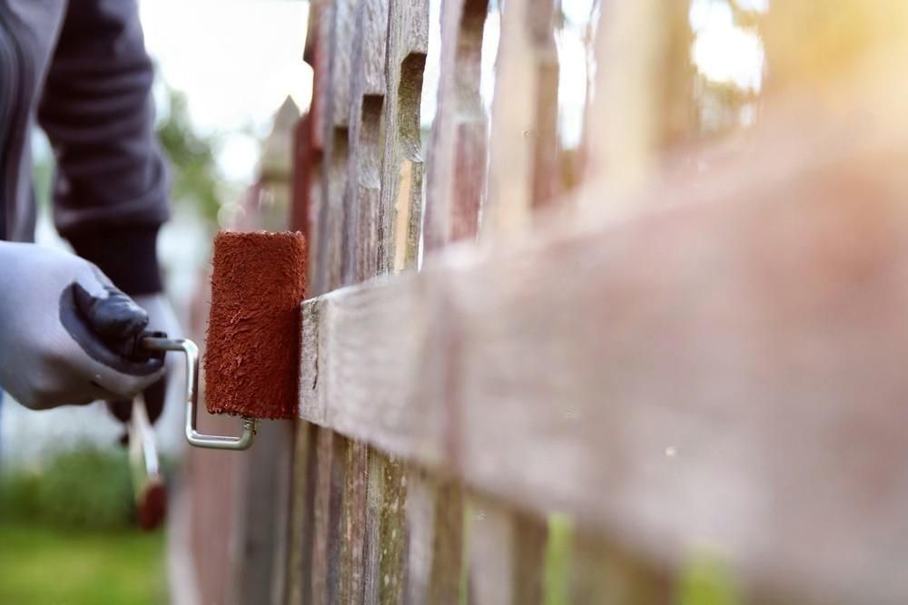 A person is painting a wooden fence with a roller brush.