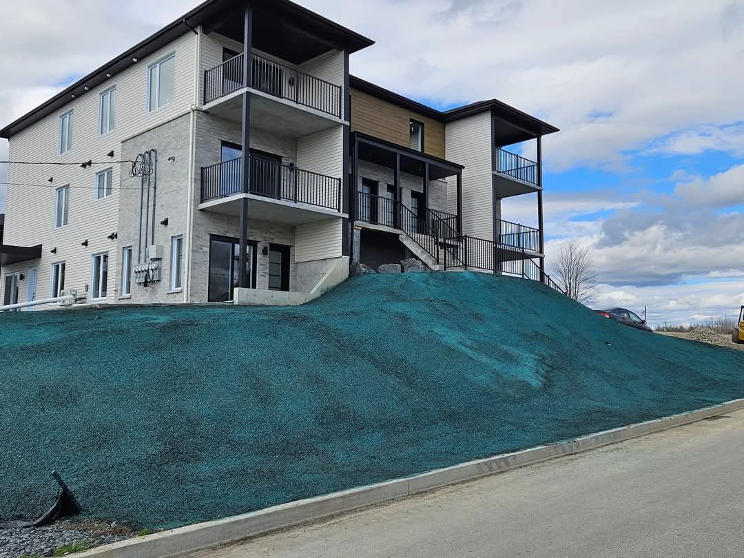 Bâtiment moderne de trois étages avec balcons, situé à flanc de colline et recouvert de végétation.