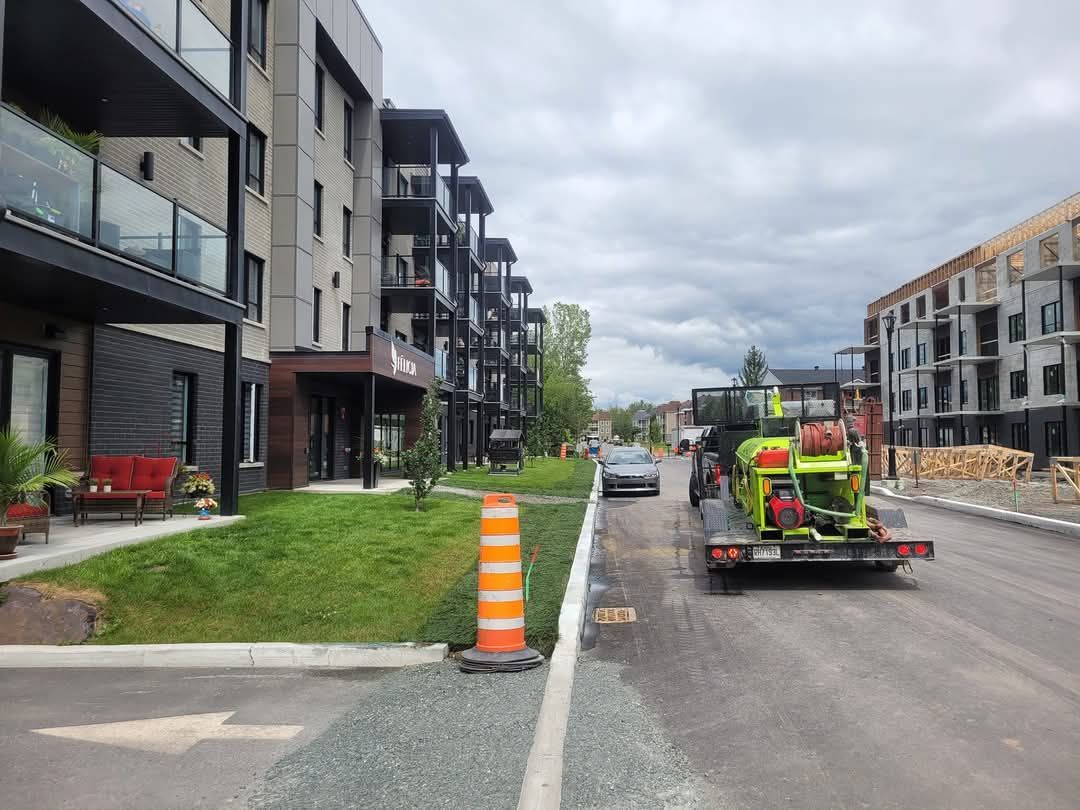 Immeubles d'appartements et chantier de construction avec un camion et une remorque sur une route. Journée nuageuse.