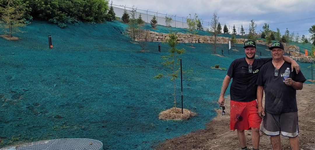 Deux hommes se tiennent devant une colline recouverte de graines hydrogéniques turquoise, avec quelques petits arbres.