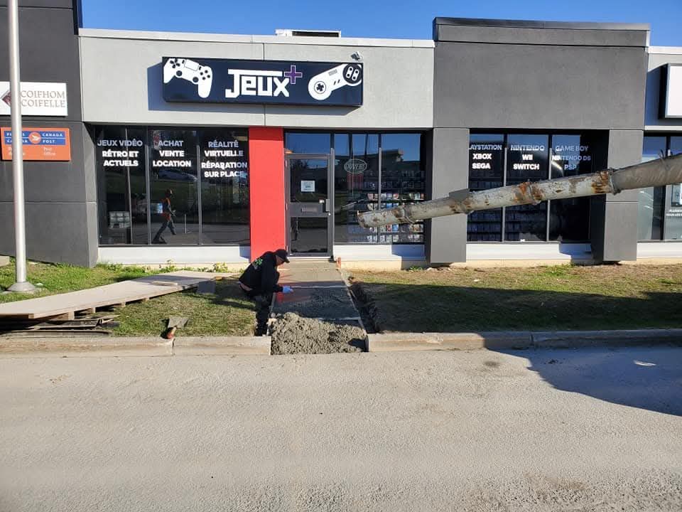 Un ouvrier du bâtiment coule du béton sur la façade d'un magasin avec une enseigne « Jeux » au-dessus de la porte.