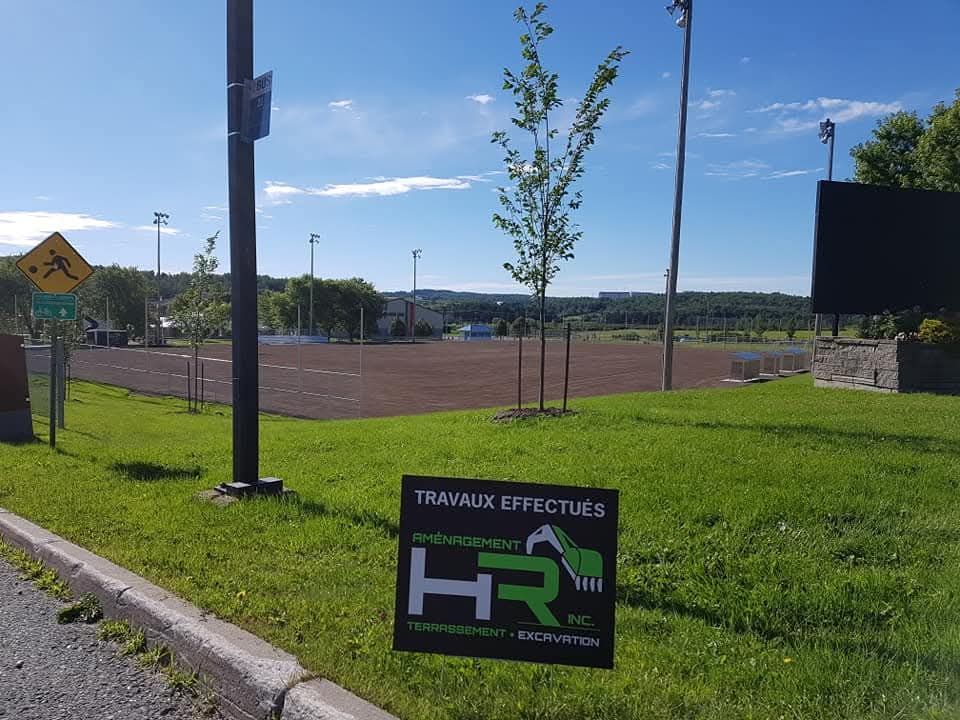 Champ avec panneau de travaux sur l'herbe. Herbe verte, ciel bleu, arbre et champ ouvert en arrière-plan.