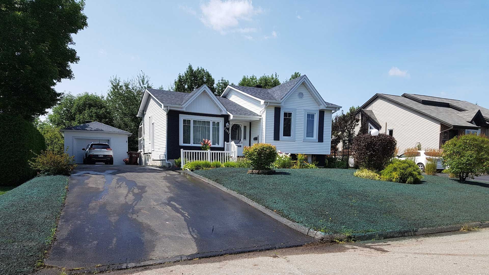 Maison blanche et noire avec garage indépendant et longue allée, par une journée ensoleillée.