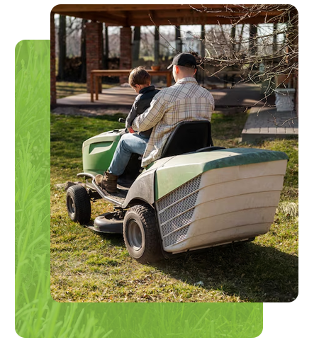 Un homme et un enfant conduisent un tracteur tondeuse vert dans une cour herbeuse.