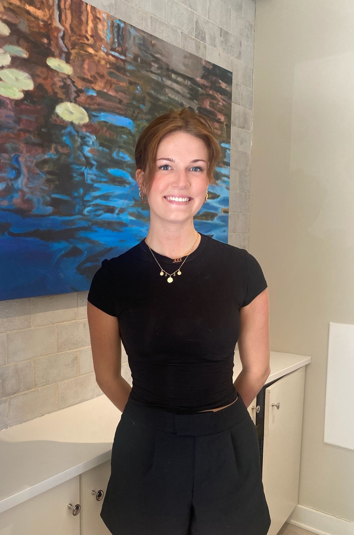 A woman in a black shirt is sitting in front of a painting.
