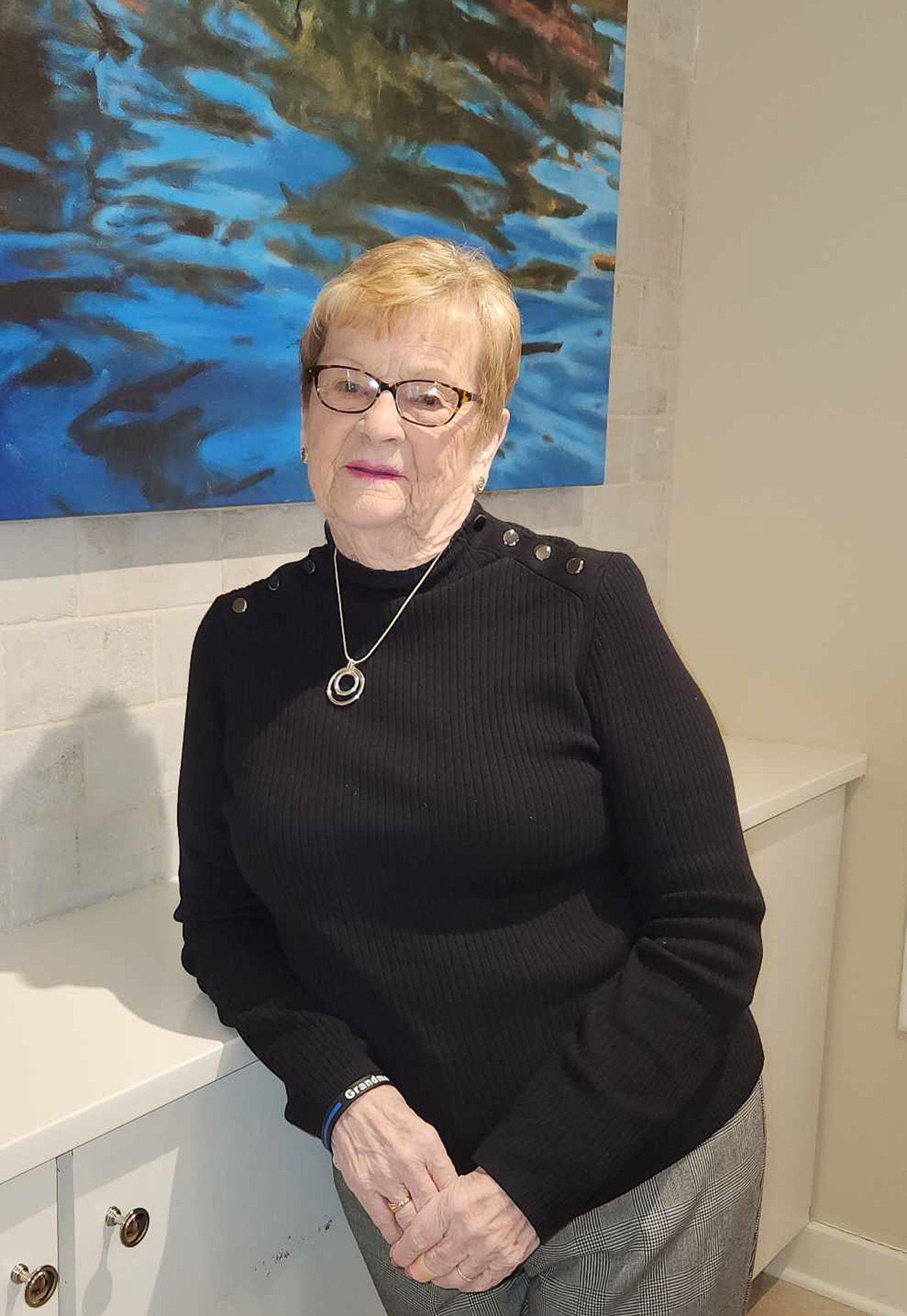 A woman wearing glasses and a black sweater is leaning against a wall.