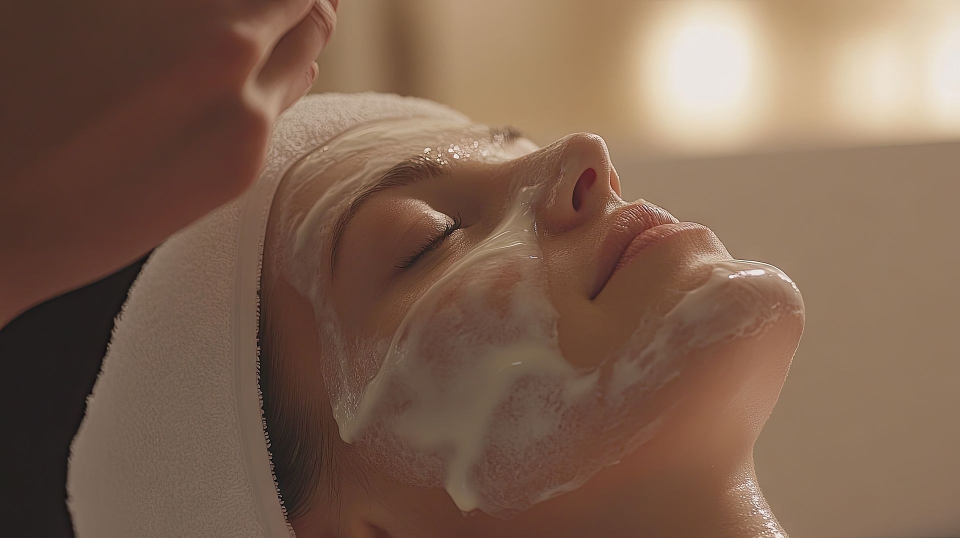 Person receiving a facial treatment with foam on their face, eyes closed, in a spa setting