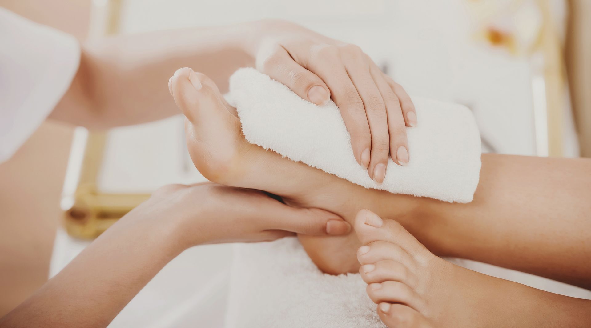 Hands gently wrapping a white towel around a foot during a spa treatment