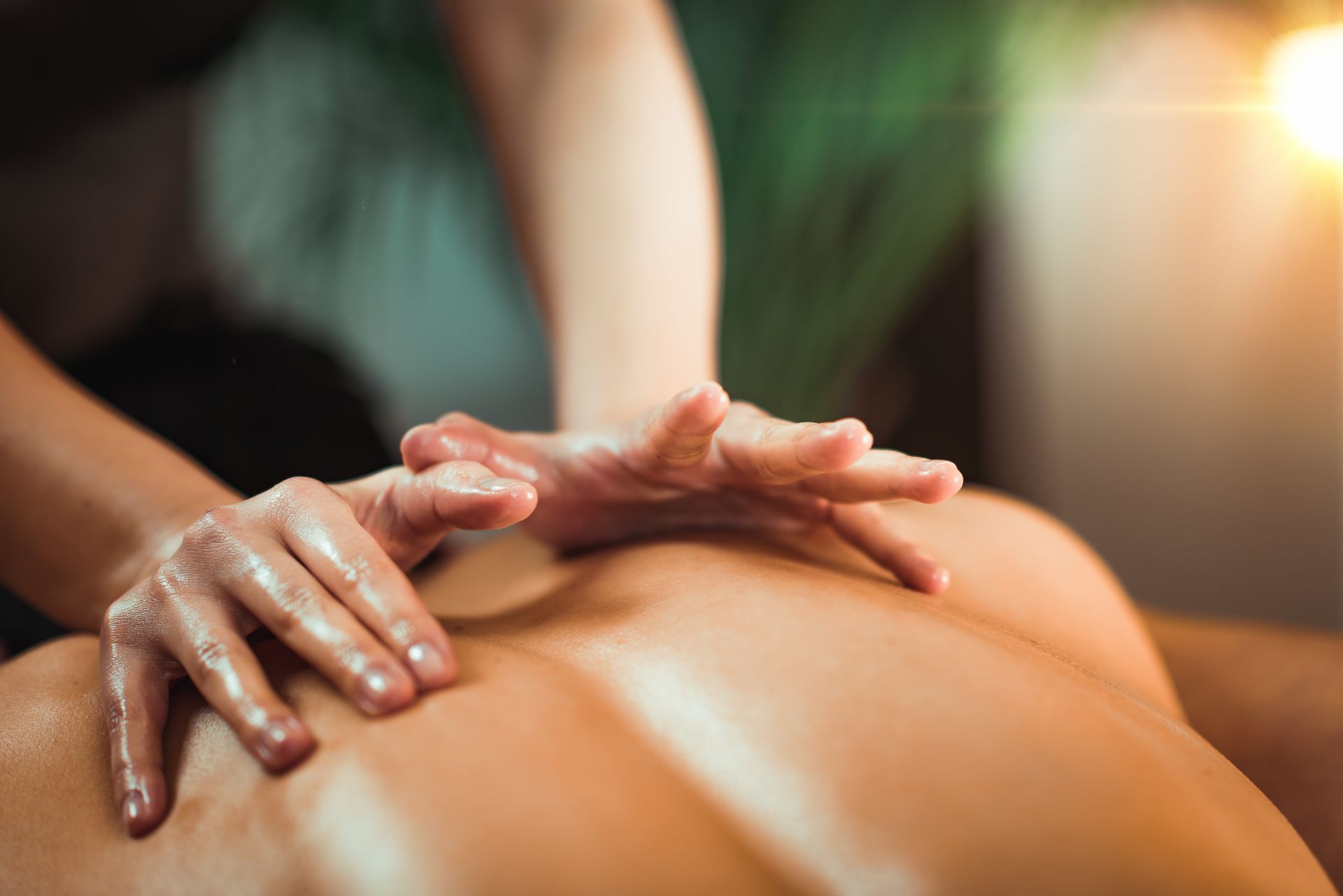 Hands massaging someone's oiled back. Soft light and green backdrop.