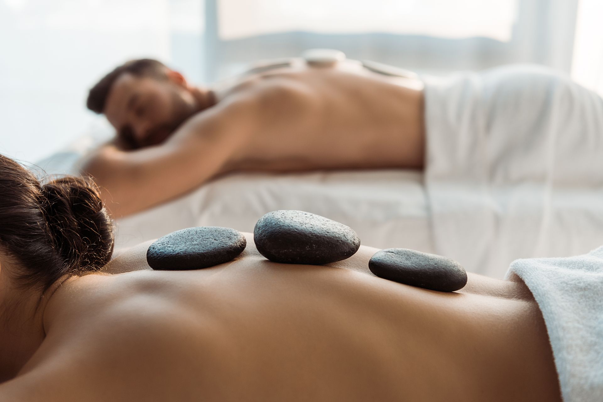 People receiving hot stone massages at a spa; dark stones on their backs.