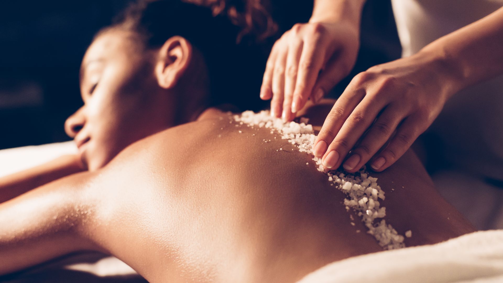 Person receiving a back massage with a crystal scrub in a spa setting