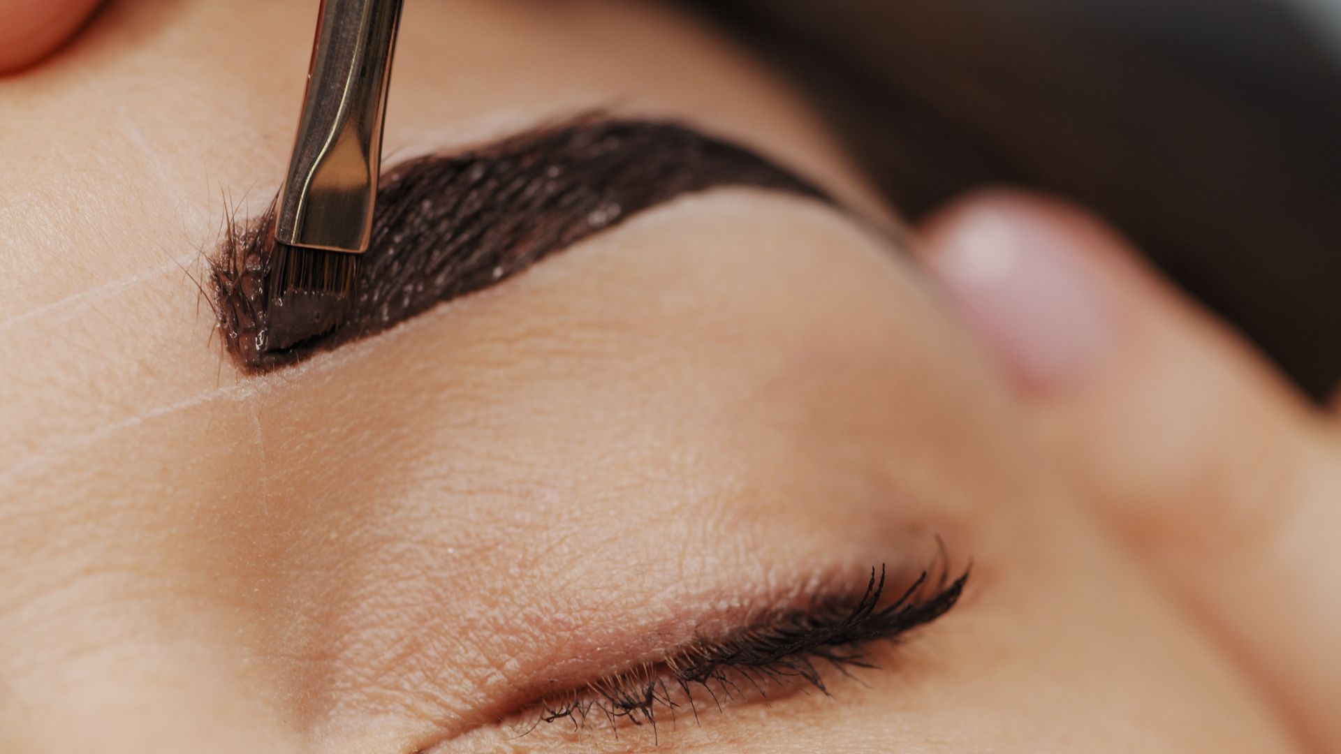 Eyebrow being dyed with dark brown dye, close-up of a person's eye and brow, beauty treatment.