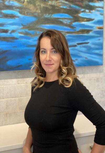 A woman in a black shirt is standing in front of a painting.