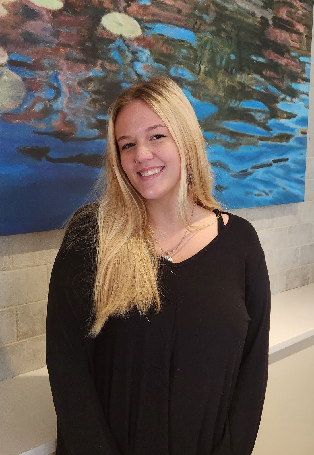 A woman in a black sweater is standing in front of a painting.