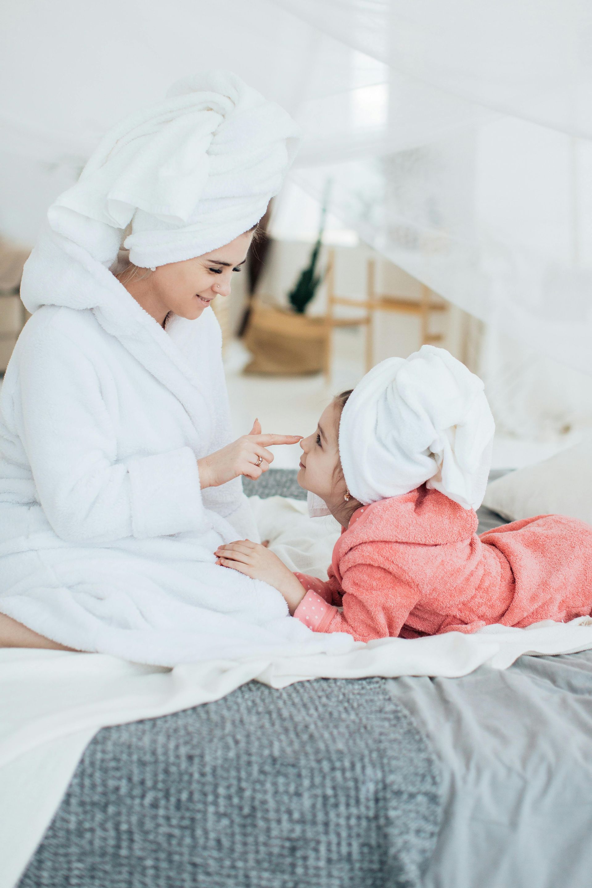 A mother and daughter are sitting on a bed with towels wrapped around their heads.