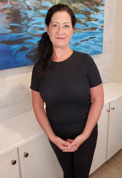 A woman in a black shirt is standing in front of a painting on a wall.