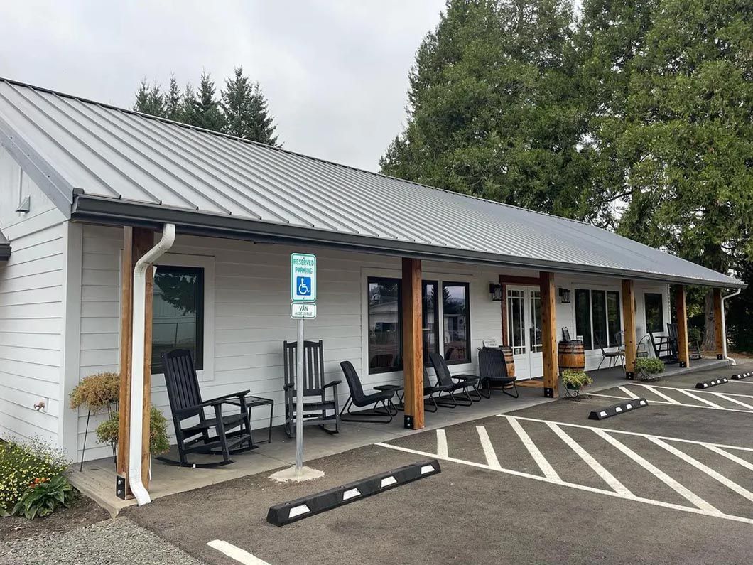 A white building with a metal roof and rocking chairs in front of it.