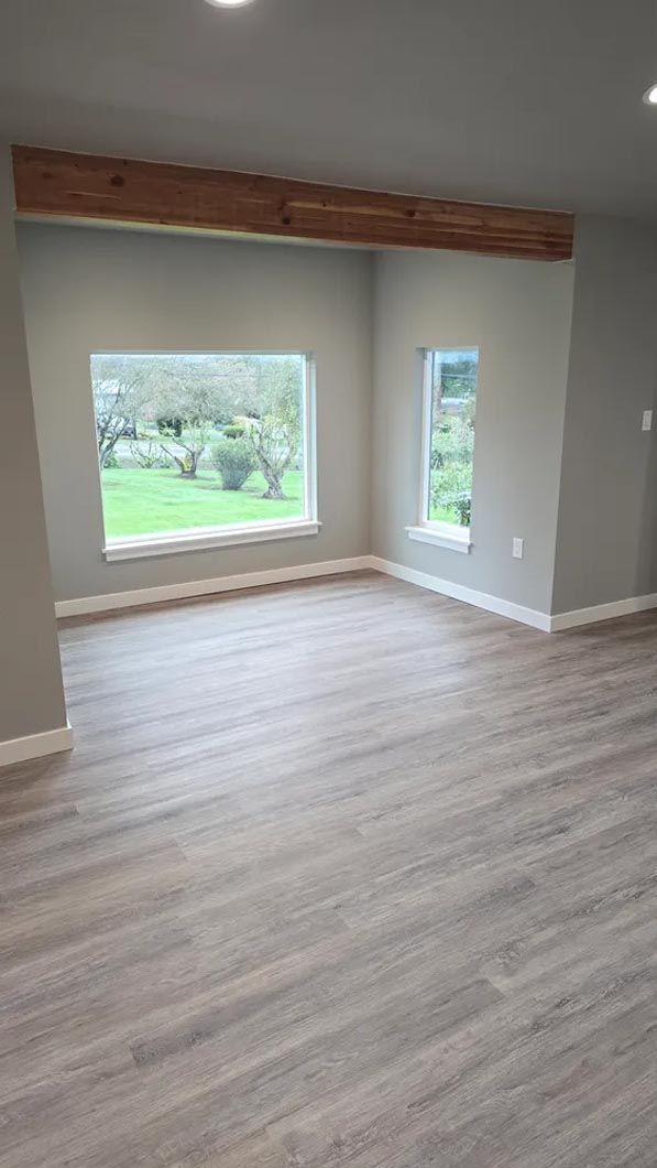 An empty living room with hardwood floors and two windows.