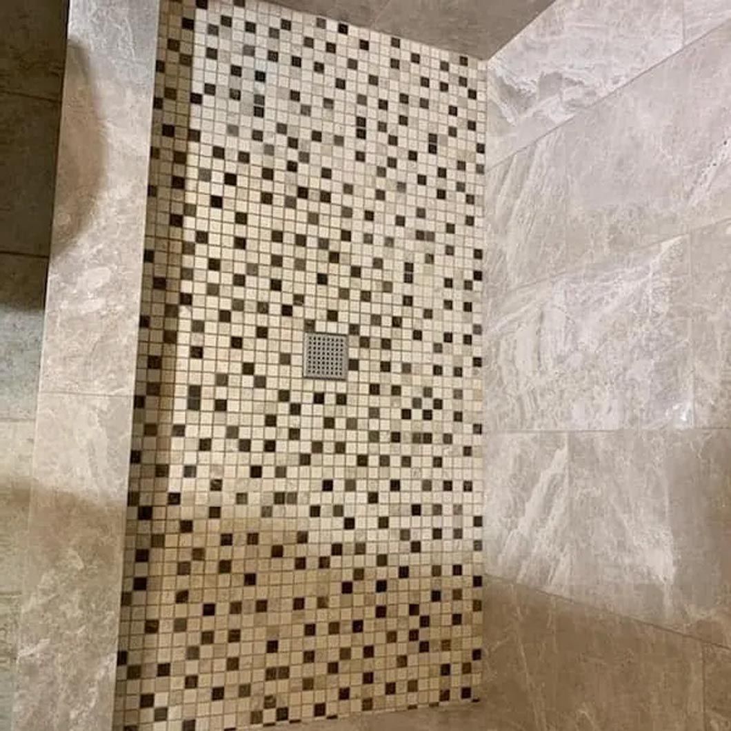 A shower stall with a mosaic tile floor and a drain.
