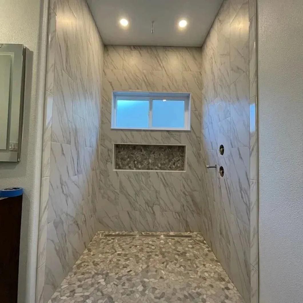 A bathroom with marble walls and a walk in shower with a window.
