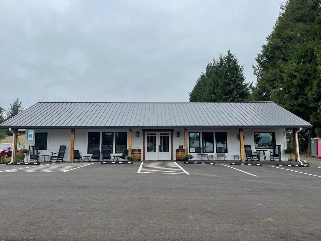 A large white building with a metal roof and a parking lot in front of it.