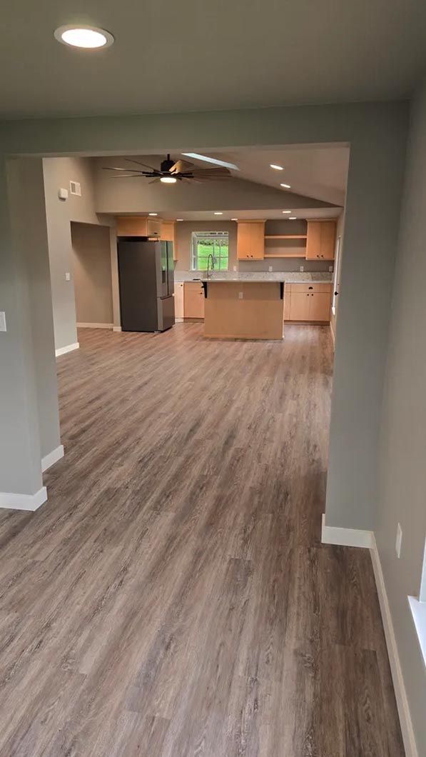 A living room with hardwood floors and a kitchen in the background.