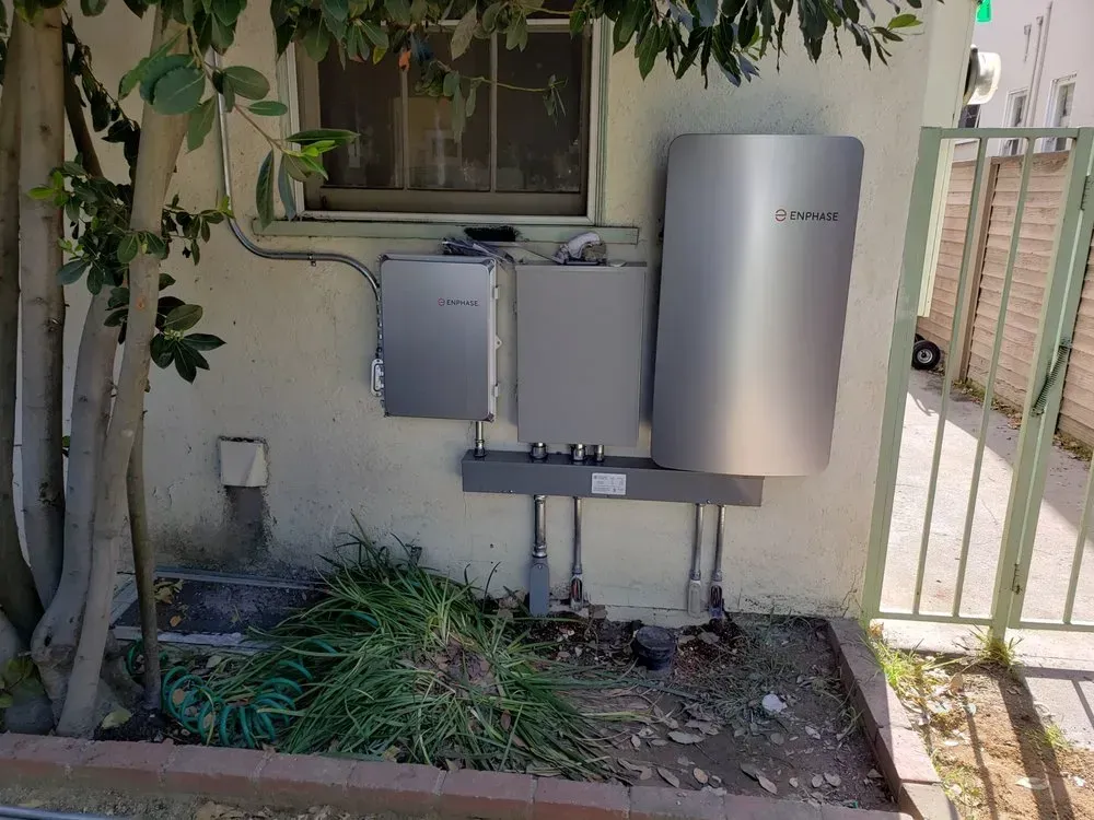A stainless steel water heater is sitting on the side of a building next to a window.